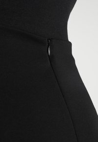 Gros plan sur une robe noire cintrée avec une texture lisse, des détails de couture et une fermeture éclair courte sur le côté gauche.