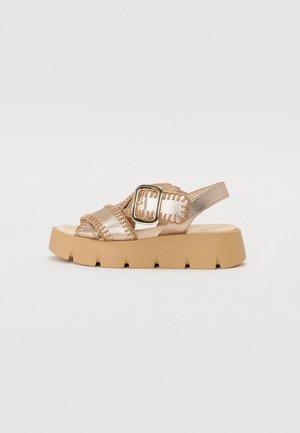 Chunky beige sandal with thick sole, wide stitching detail, large square buckle, and back strap for support.