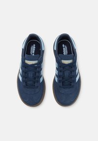 Navy blue suede sneakers with light blue accents and three stripes. Features lace-up design and textured brown rubber sole. Gold detailing present.