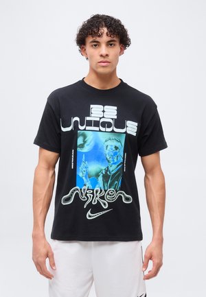 Młody mężczyzna z kręconymi włosami w czarnej, graficznej koszulce Nike z napisem "Be Unique" i niebieskawym futurystycznym portretem.
