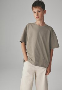 Olive zelené oversized tričko z mäkkého bavlneného materiálu s okrúhlym výstrihom, krátkymi rukávmi a voľným strihom, skombinované s svetlými širokými nohavicami.