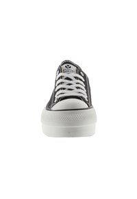 Zapatilla de lona negra con puntera de goma blanca, cordones blancos y suela de goma texturizada. Presenta el logo en la lengüeta y costuras en contraste.