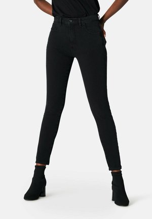 Jeans skinny neri a vita alta realizzati in denim, con tasche frontali e chiusura con bottone, abbinati a stivali neri per caviglia.