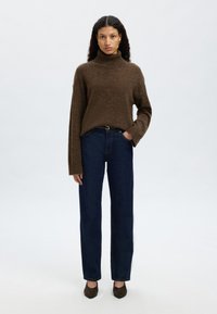 Barna garbó puha, texturált kötött anyagból, sötétkék egyenes szárú farmerrel és sötétbarna, hegyes orrú magassarkúval párosítva.
