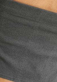 Detailní záběr na šedou látku s vertikálním a horizontálním šitím na světlém pozadí pleti.