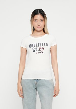 Valge lühikeste varrukatega T-särk, mille esiküljel on mitmevärviline tekst "Hollister Co. 1922 So-Cal". T-särk on valmistatud pehmest puuvillast ja on kehakujuline.