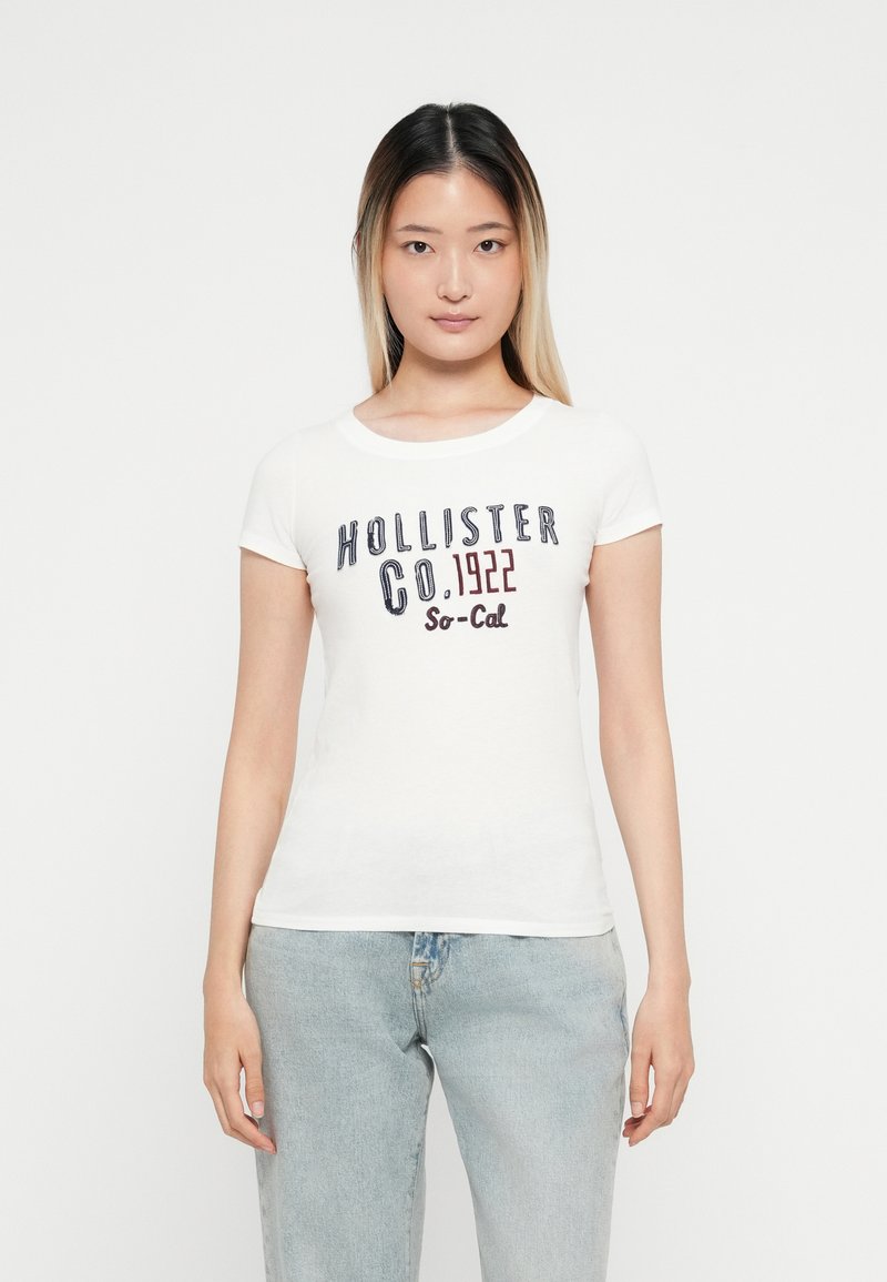 Hvit t-skjorte med korte ermer og flerfarget tekst "Hollister Co. 1922 So-Cal" på fronten, laget av mykt bomullsmateriale, tettsittende design.