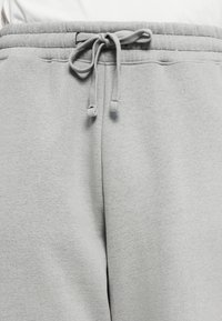 Nærbillede af grå sweatpants med elastisk talje og bundet snøreknude foran i midten.