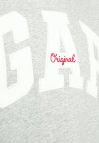 Grå hettegenser med hvit, oversized tekst som skriver "GARA" og rød brodert "Original." Myk tekstur, avslappet design og rund hals.