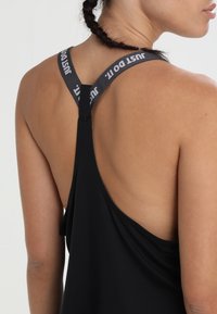 Top atletico nero senza maniche con design racerback, caratterizzato da un logo grigio "just do it" sulle spalline e uno scollo posteriore basso. Tessuto morbido e traspirante.