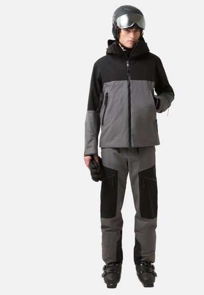 Zweiteiliges Skianzug in Schwarz und Grau, bestehend aus einer Jacke mit Reißverschluss und Hosen mit Seitentaschen, gefertigt aus einem strukturierten, wetterfesten Stoff.