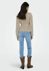 Beežist kootud kampsun õõnesmustritega ja vööst seotud, sobitatud hele siniste teksade ning pruunide seemisnahast lõunapõhja saapastega.