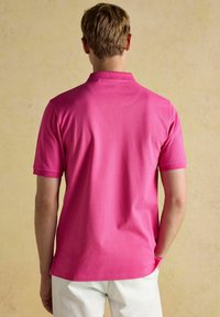 Lühikeste varrukatega polo-särk erkoranžist puuvillast, millel on soonikkoes krae, sile tekstuur ja sirge äär, kantud valgete pükstega.