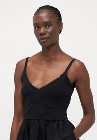 Top corto de punto negro con tirantes ajustables, presenta un escote en V y un cuerpo texturizado. La parte inferior tiene un diseño fruncido para un ajuste relajado.