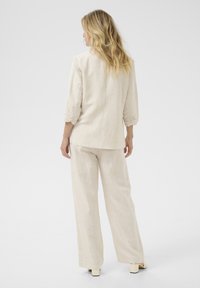 Beige linnen blazer met driekwartmouwen, gecombineerd met bijpassende wijde broek, heeft een relaxte pasvorm en een minimalistisch design.