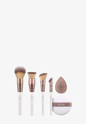 Ensemble de cinq pinceaux de maquillage avec manches blancs et accents en or rose. Comprend un pinceau à fond de teint, un pinceau à anti-cernes, une éponge à estomper et une houppette à poudre.