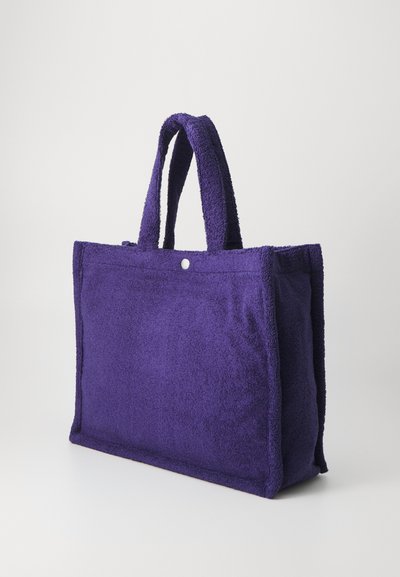 Lila Handtasche aus Frottee mit kurzen, plüschigen Tragegriffen. Rechteckige Form, ausgestattet mit einem Druckverschluss und einer sauberen, strukturierten Oberfläche.