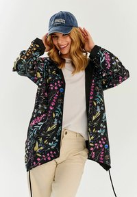 Čierna kvetinová bunda s farebnými vzormi v ružovej, modrej a zelenej; má zips vpredu a šnúrku na spodnom okraji. Model nosí džínsovú čiapku.