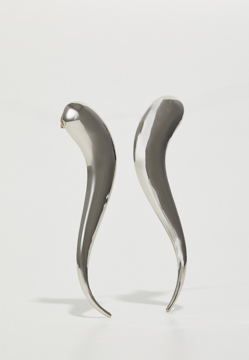Metalické strieborné náušnice s hladkým, predĺženým tvarom, ktoré majú hladký povrch a zakrivený dizajn zužujúci sa k špičke.