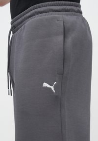 Szare spodnie dresowe z sznurkiem w pasie, bocznymi kieszeniami i białym logo Puma na lewej nogawce. Wykonane z miękkiego materiału o gładkiej fakturze.