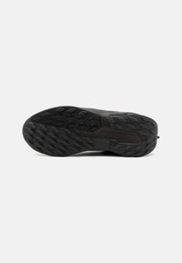 Semelle de chaussure de sport noire avec une surface texturée et à motifs. Présente des crampons profonds pour l'adhérence, des bords renforcés et des détails de marque.
