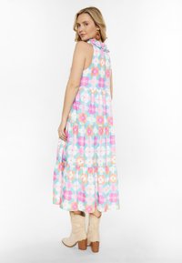 Maxikleid mit floralem Muster, das einen hellblauen Hintergrund, mehrfarbige Blumenmuster, einen gerafften Kragen und einen gestuften Rock zeigt. Kombiniert mit beigen Cowboy-Stiefeln.