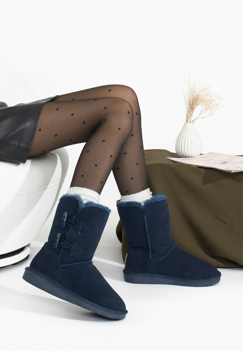 Botas de ante azul marino con forro de piel sintética, que presentan dos botones decorativos y una suela texturizada, combinadas con unas medias negras con lunares.