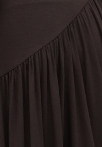 Σκούρο καφέ ύφασμα με διαγώνια ραφή που μεταβαίνει σε μαζεμένη, πλισέ υφή κάτω από τη ραφή.