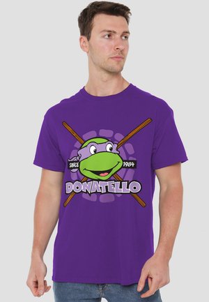 Purple cotton t-shirt featuring a graphic of Donatello, a turtle character, with a green face and crossed nunchaku. Worn by a male model.