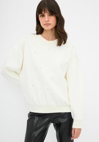 Bílá mikina se zakulaceným výstřihem, dlouhými rukávy a ozdobená malými, rozházenými stříbrnými cvočky. Nosit s černými kalhotami z umělé kůže.