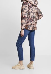 Chaqueta acolchada con un patrón floral rosa, combinada con jeans azules y zapatillas beige. La chaqueta tiene capucha y un diseño ajustado.
