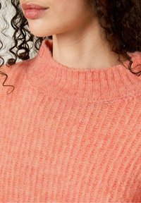 Ribbed, pehmeä neulepaita vaalean persikan värissä, jossa on korkea kaulus. Paidassa on tekstuuripinta ja hienovaraisia sävyjä kauttaaltaan.