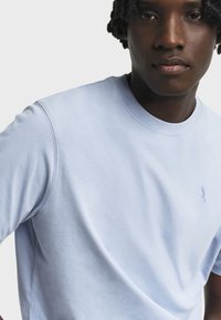 T-shirt in cotone azzurro chiaro con collo rotondo e maniche corte, con un piccolo logo ricamato sul petto. Texture liscia.