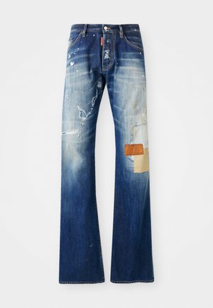Denim jeans with a faded blue wash, distressed details, visible patches, and raw hems. Features a branded tag and contrasting fabric accents.