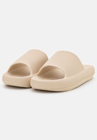 Béžové sandály na slip-on s texturovaným povrchem a širokým popruhem; gumový materiál; otevřená špička; plochá podrážka.