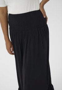 Black skirt with a smocked waist, flowing silhouette, made from soft fabric, featuring gathered texture and a ruffled hem.