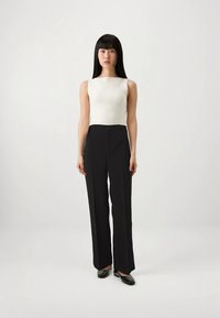 Svarte vide bukser kombinert med en beige ribbestrikket ermeløs topp. Materialet er glatt, med rene linjer og en skreddersydd passform.