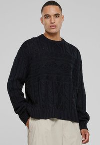 Pull en tricot noir avec un motif en relief de torsades, col rond et poignets et ourlet côtelés. Coupe oversize avec une silhouette décontractée.
