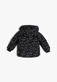 Sort pufferjakke med hvidt prikket mønster, der har hætte, elastiske manchetter og en quiltet design for isolering.