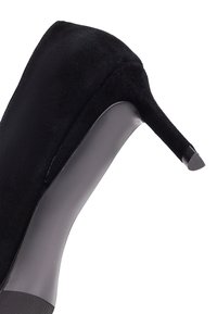 Chaussure à talon haut en suède noir avec un bout pointu élégant et un accent glossy noir sur le talon ; présente un profil latéral lisse.