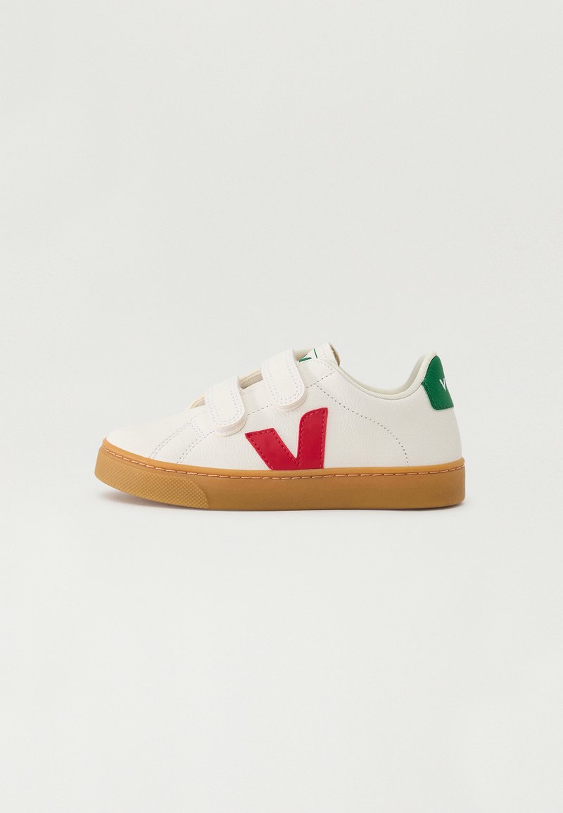Baskets blanches avec des bandes Velcro, logo 'V' rouge, accent vert sur le talon et une semelle en caoutchouc beige. Matériau lisse, design à bout rond.