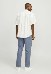 Camisa de manga corta blanca a rayas con un dobladillo curvado, combinada con pantalones tapered azul claro y zapatillas blancas, vista desde la parte de atrás.