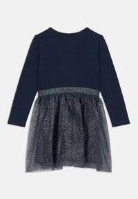 Φόρεμα μακρυμάνικο με μπλε πάνω μέρος και διαφανή, γυαλιστερή φούστα από τούλι, επικαλυμμένη από ένα στερεό μπλε υπόστρωμα, με γυαλιστερή λεπτομέρεια στη μέση.