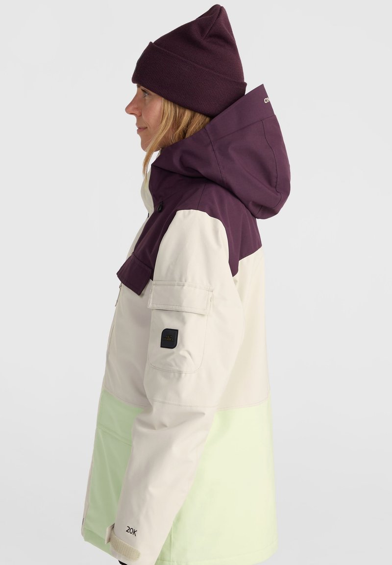 Kurtka w kolorze blokowym z fioletowym kapturem, kremową górną częścią i miętowozielonym dolnym fragmentem. Wykonana z trwałego materiału z kieszenią na zamek.