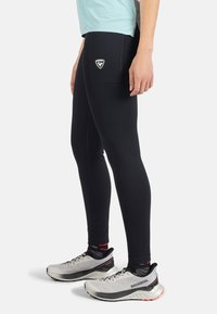 Mustat leggingsit, joissa on tiukka muotoilu, takana tasku ja logo. Yhdistettyinä hopeisiin urheilukenkiin ja teksturoituihin mustiin sukkiin.