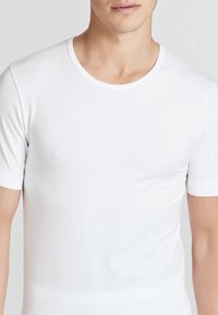 T-shirt bianca a maniche corte con collo rotondo, realizzata in tessuto liscio, design aderente, caratterizzata da cuciture minime e uno stile pulito e semplice.