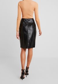 Jupe crayon en cuir noir avec un motif texturé effet serpent, longueur mi-mollet, associée à un haut à manches longues côtelé. Chaussures à talons avec bride à la cheville.