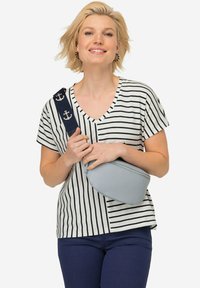 Top a righe con scollo a V in crema e blu navy, abbinato a una borsa ovale di colore blu chiaro con cerniera, tenuta da una tracolla con motivo ancorato.