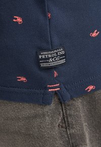 Polo bleu marine avec de petits motifs de homards rouges, doté d'une étiquette de marque noire et blanche cousue près de l'ourlet, et en tissu texturé.