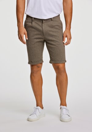 Dunkelkhakifarbene, maßgeschneiderte Shorts aus einem strukturierten, atmungsaktiven Stoff, mit umgeschlagenen Säumen und einem klassischen Bund, kombiniert mit weißen Sneakern.